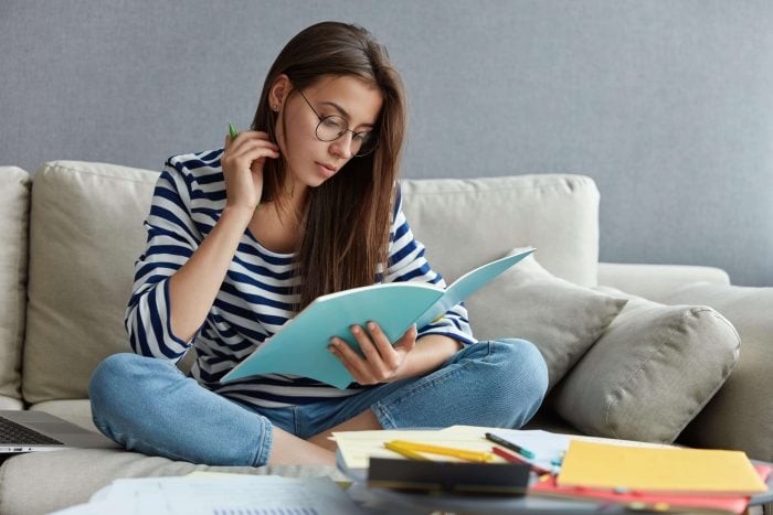 Woman sitting on a couch and completing Korean exercises on her notebook