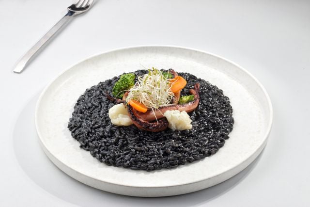 Crni rižot, Croatian black risotto with squid ink and seafood, served with vegetables.