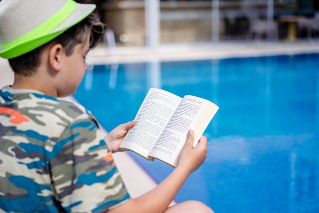 Child reading a book by the pool during a summer language-learning break.